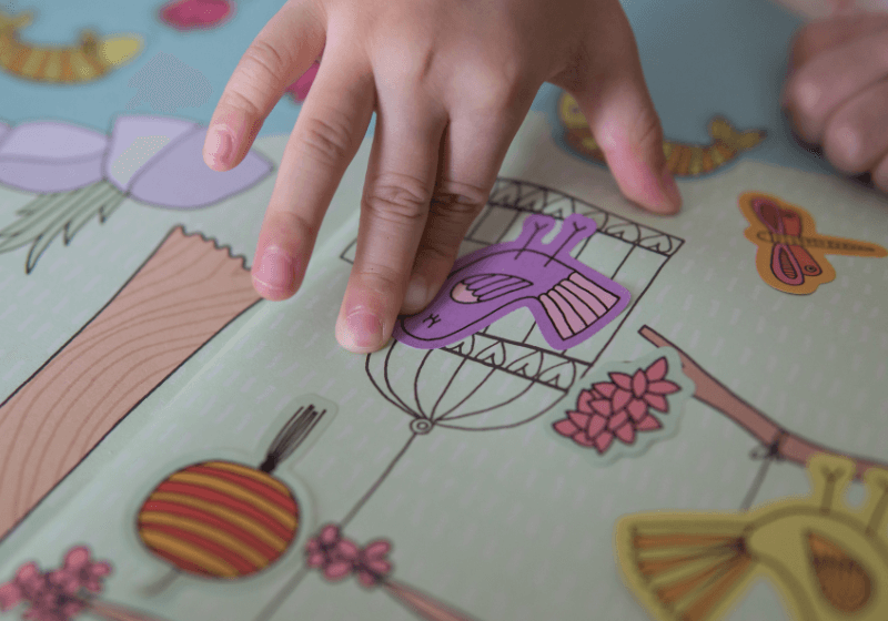 libros de pegatinas. Niño colocando pegatina en un libro de actividades con dibujos coloridos de animales y flores