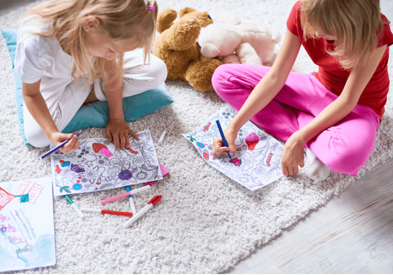 libros de colorear para niños. Niñas coloreando libros en el suelo con rotuladores, rodeadas de dibujos y colores vivos