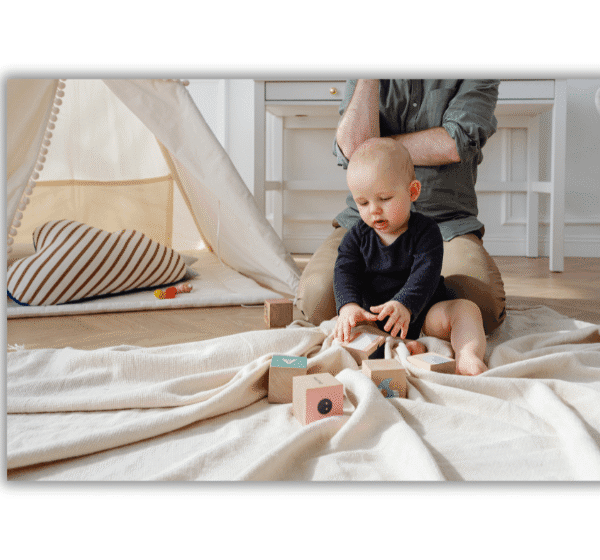 Juguetes Montessori para bebés. Bebé jugando con bloques Montessori sobre una manta, acompañado por un adulto, en un ambiente preparado tipo Montessori.